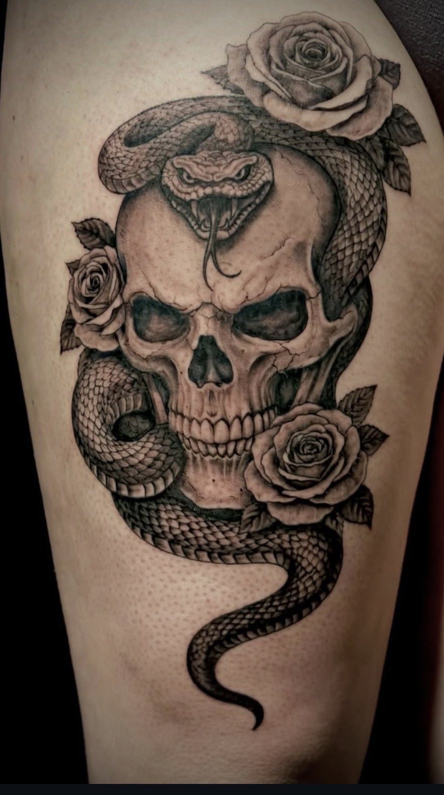 Tattoo van een schedel met een slang en rozen op het bovenbeen