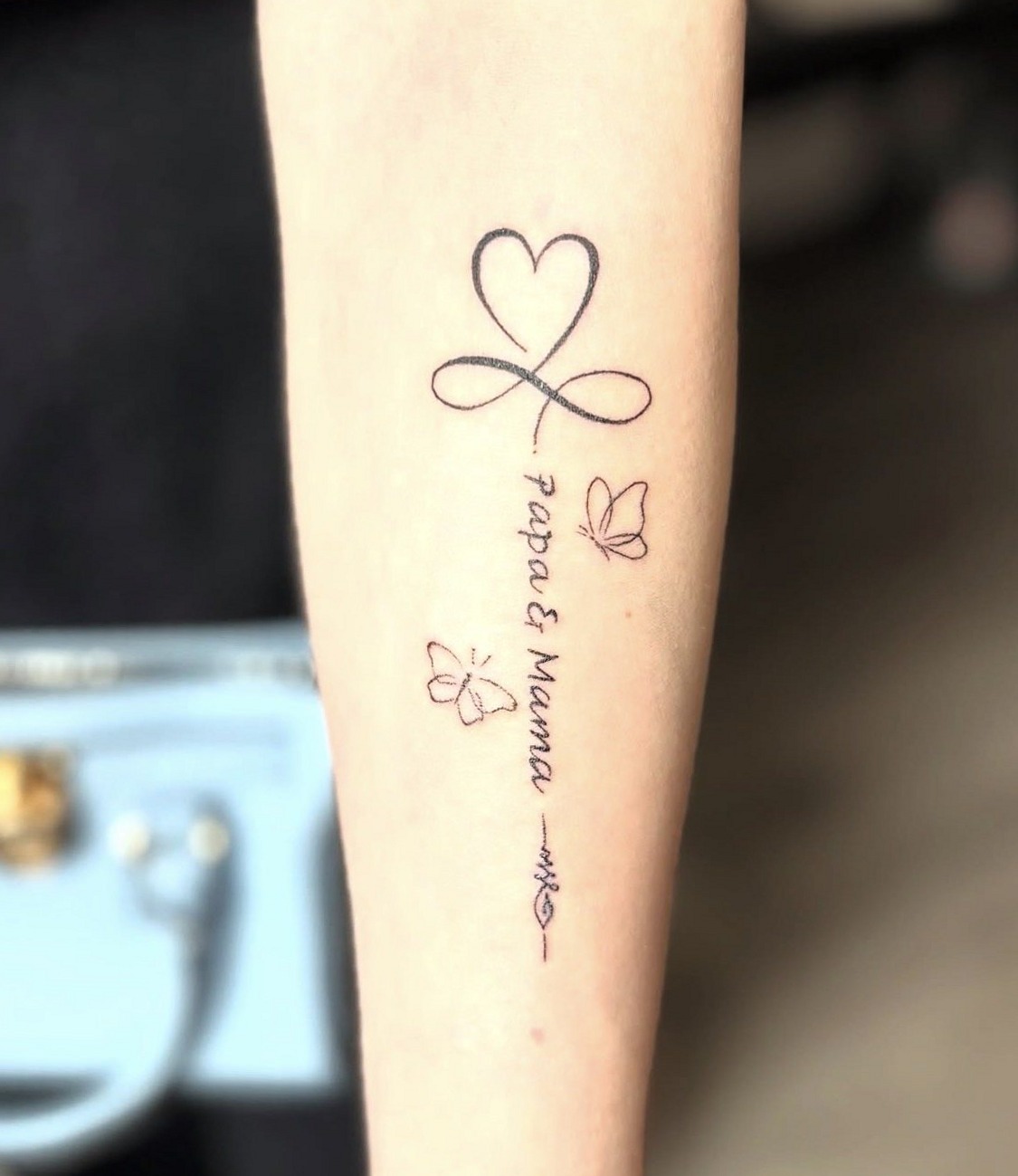 Fijne tattoo met de woorden Papa & Mama, een hart en vlinders op de onderarm