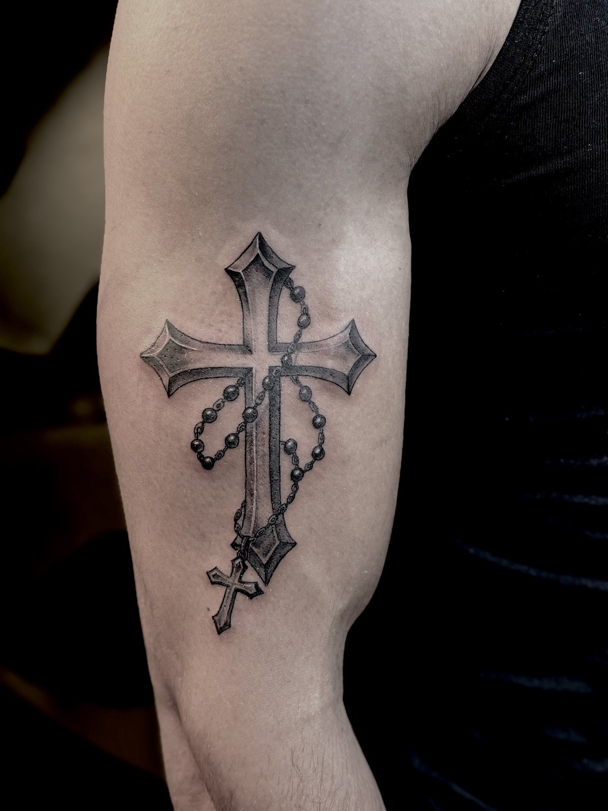 Tattoo van een kruis met een rozenkrans op de bovenarm